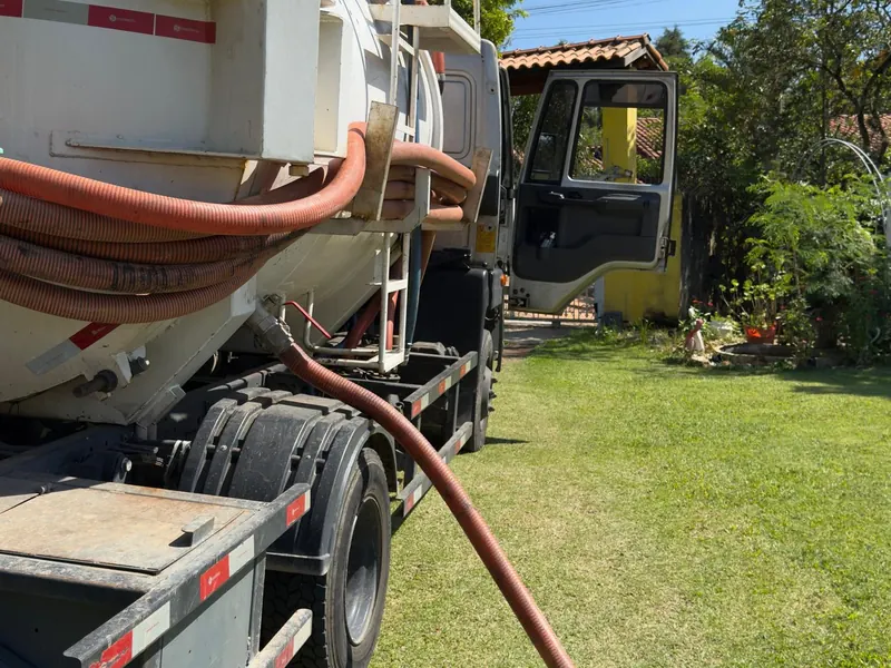 Caminhão limpa fossa com mangote estendido em chácara